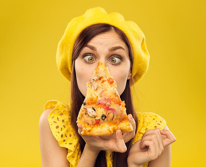 funny woman in a beret hungry eats pizza on a yellow portraite background