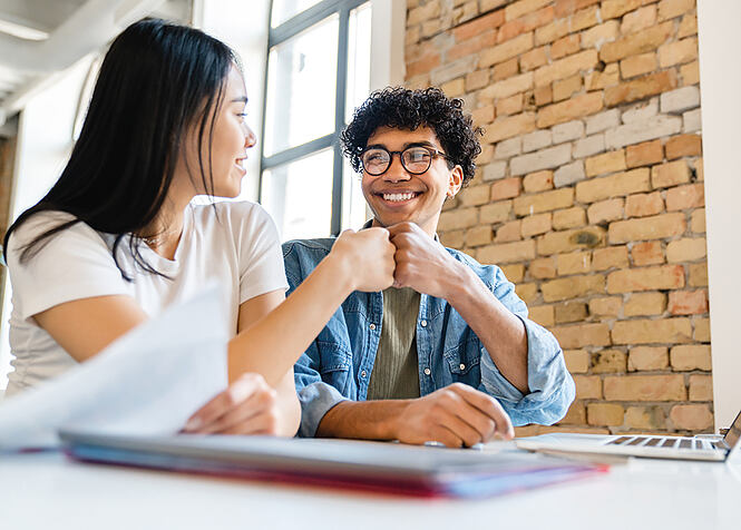 Cheerful young colleagues business partners friends students classmates giving fist bump during working process. People working studding doing home work create start up together in loft cafe